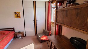 Quarto com cama, escrivaninha, cadeira, estante de livros e radiador.