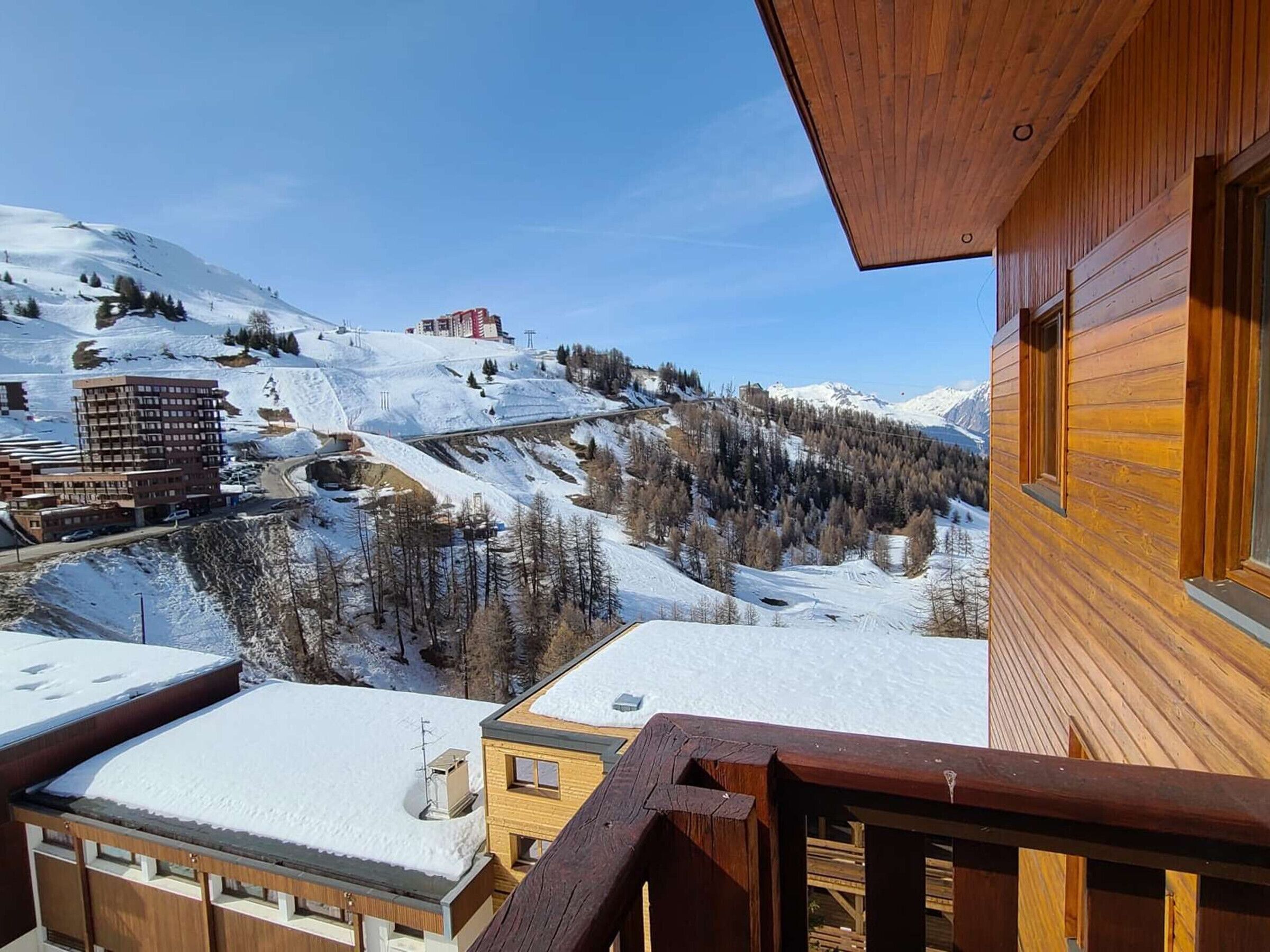 Eine Holzhütte mit einem Balkon mit Blick auf eine verschneite Berglandschaft, einschließlich einer Seilbahn und Gebäuden.