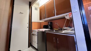 Uma cozinha compacta com fogão, forno e pia, com armários de madeira e cafeteira.