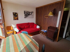 A room with a red sofa, a wooden cabinet, a small table with a lamp, and two chairs. - Functional apartment, bright view - 4 guests (La Plagne)
