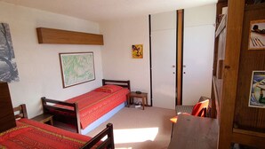 Quarto pequeno e compacto com uma cama de solteiro, uma mesinha e um guarda-roupa.