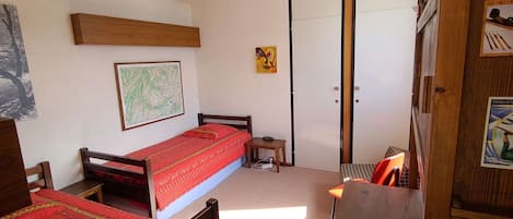 Una habitación pequeña y funcional con una cama individual, una mesita y un armario.