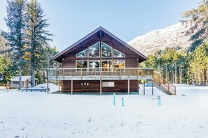 A wooden cabin with a balcony, surrounded by snow and trees.