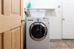 A front-loading washing machine in a laundry room with a wooden door and a white wall.