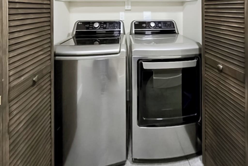 A laundry room with two stainless steel appliances, one dryer and one washer, enclosed by wooden panel walls.