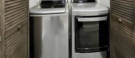 A laundry room with two stainless steel appliances, one dryer and one washer, enclosed by wooden panel walls.