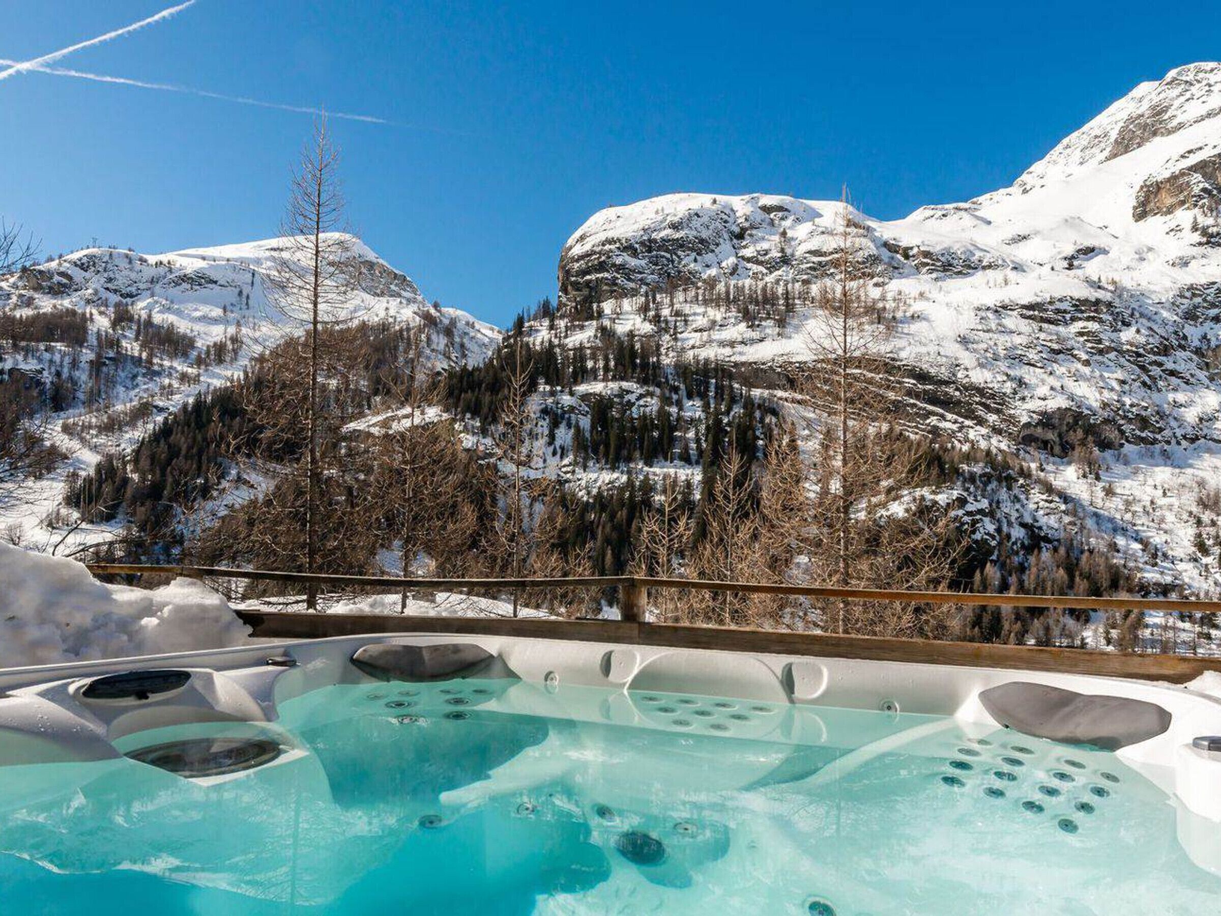 A hot tub with a mountain view, surrounded by snow-covered terrain and trees.