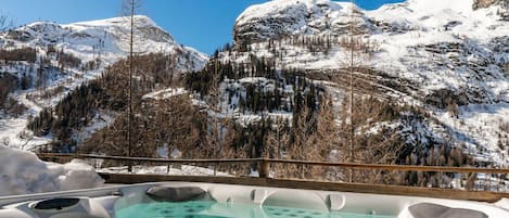 A hot tub with a mountain view, surrounded by snow-covered terrain and trees.