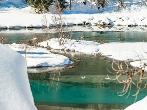 Eine natürliche Landschaft mit einem Fluss, schneebedecktem Boden und Bäumen.