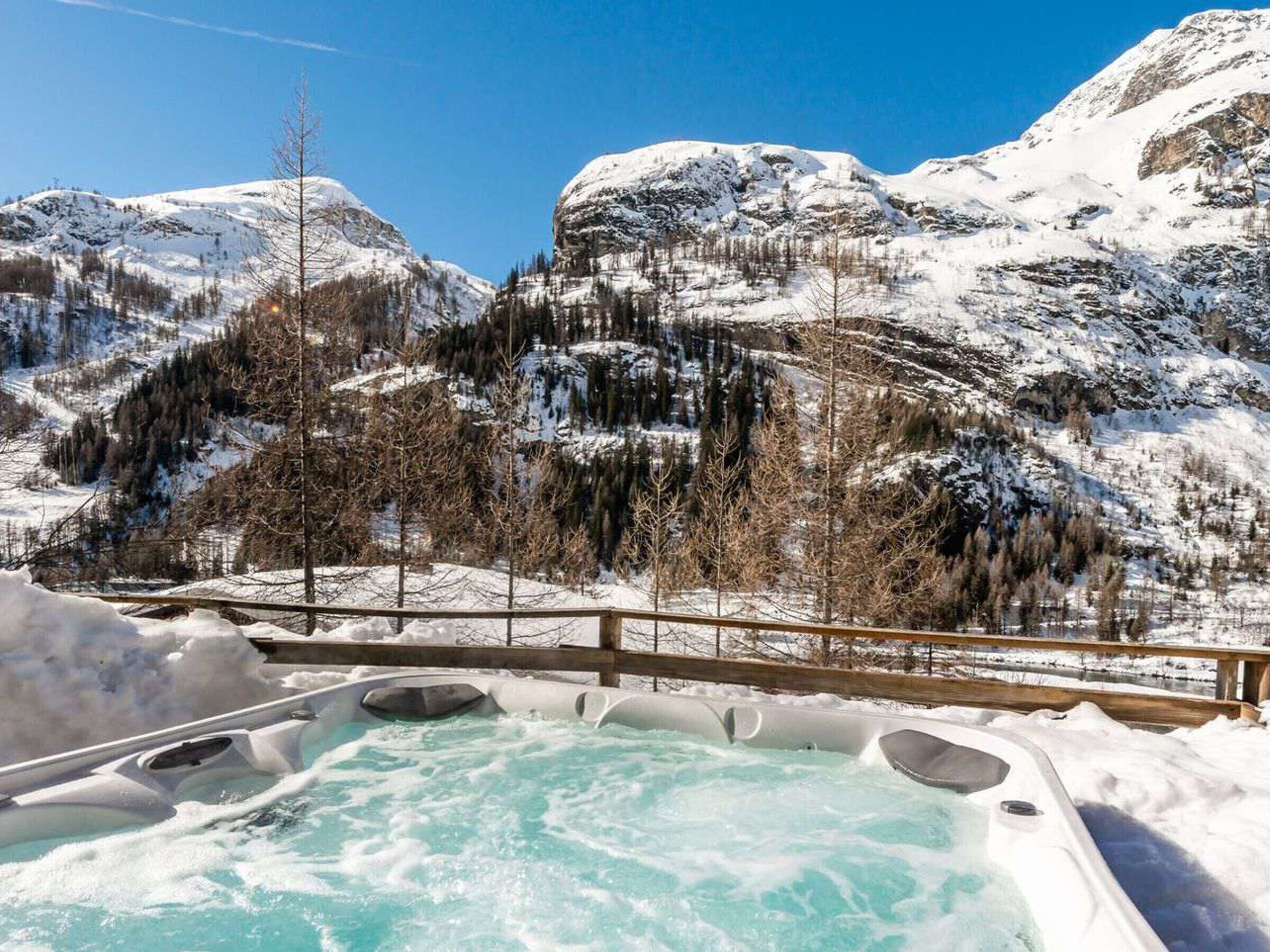 Een hottubgedeelte met een houten terras en uitzicht op besneeuwde bergen.