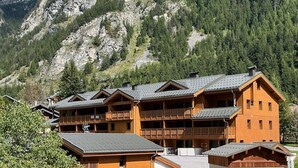 Una cabaña de madera de varios pisos con balcones, con montañas al fondo.