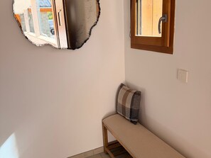 Ein Zimmer mit einer Holzbank, einem an der Wand befestigten Spiegel und einem Fenster mit Holzrahmen.