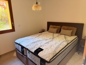 Een slaapkamer met een bed, een raam en een hangende lamp.