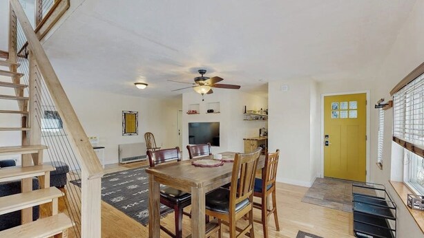 A dining area with a wooden table and chairs, a ceiling fan, and a yellow door.