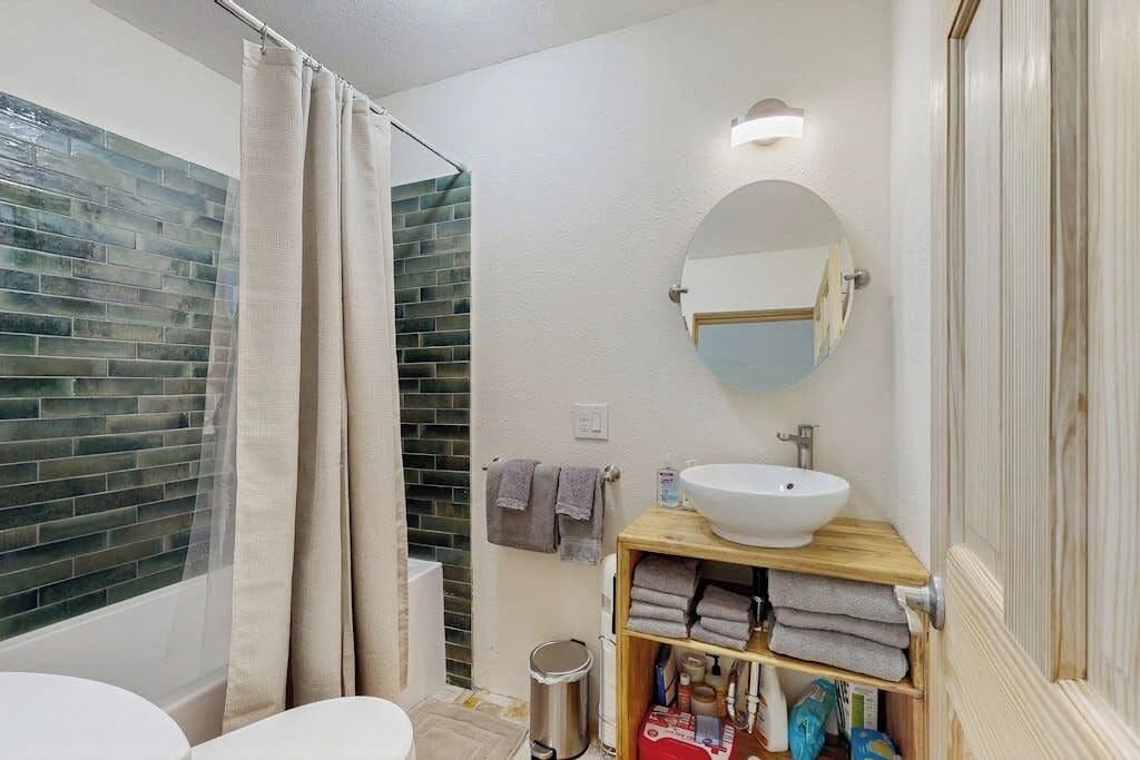 A bathroom with a white sink, a wooden shelf with towels, a mirror, and a shower curtain.