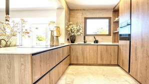 A modern kitchen with wooden cabinets, a marble countertop, and a window providing natural light. - Villa in Xabia, Splendid View and Pool (Javea)