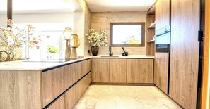 A modern kitchen with wooden cabinets, a marble countertop, and a window providing natural light. - Villa in Xabia, Splendid View and Pool (Javea)
