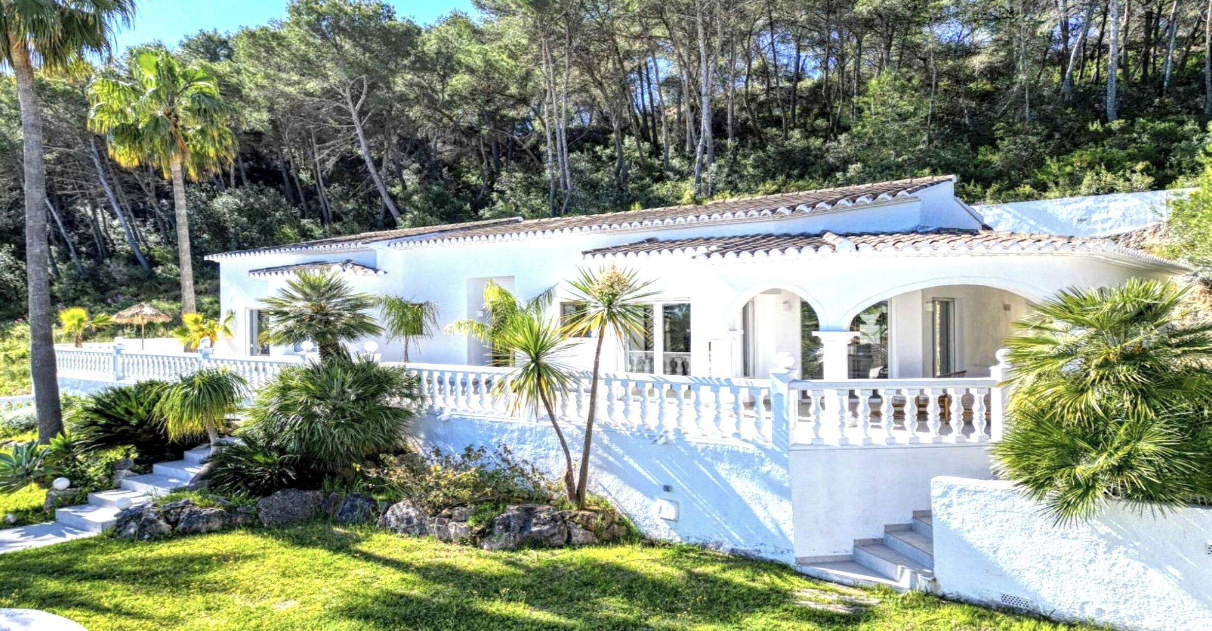 A white building with a tiled roof, surrounded by lush greenery and palm trees.