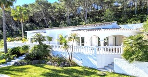 A white building with a tiled roof, surrounded by lush greenery and palm trees. - Villa in Xabia, Splendid View and Pool (Javea)