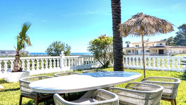 An outdoor seating area with a table and chairs, a thatched umbrella, and a view of the sea. - Villa in Xabia, Splendid View and Pool (Javea)