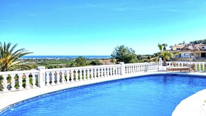A swimming pool with a white balustrade, a view of the sea, and a building with a thatched roof. - Villa in Xabia, Splendid View and Pool (Javea)