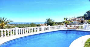 A swimming pool with a white balustrade, a view of the sea, and a building with a thatched roof. - Villa in Xabia, Splendid View and Pool (Javea)