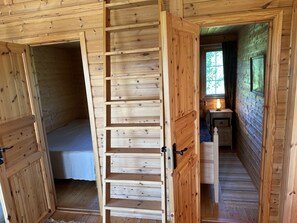 Interior de madera con cama tipo loft, una escalera y una pequeña mesa con lámpara.