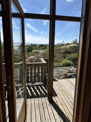 Una terraza de madera con barandilla que conduce a un vidrio que da a una vista panorámica de un lago y montañas.
