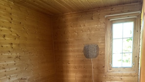 A room with a single bed, a small wooden nightstand, and a window with a view of greenery.