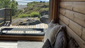 A wooden cabin with a large window overlooking a rocky landscape and a distant mountain range.