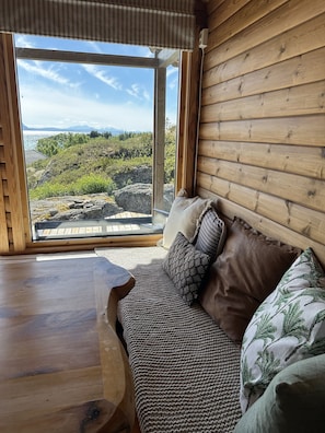 Un interior de madera con un sofá frente a un ventanal que da a un paisaje natural.