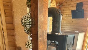 A rustic wooden interior with a traditional wood-burning stove, a woven basket, and a wooden barrel.