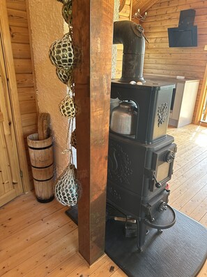 A rustic wooden interior with a traditional wood-burning stove, a woven basket, and a wooden barrel.