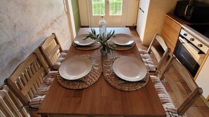 A dining room with a wooden table set for four, a kitchen with a stove and microwave, and a view through a door to a balcony. - Gîte des Tulipes de Bray (Neufchâtel-en-Bray)