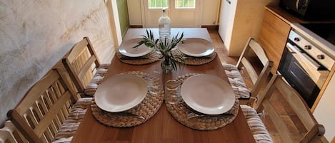 A dining room with a wooden table set for four, a kitchen with a stove and microwave, and a view through a door to a balcony.