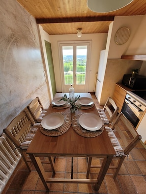 Comedor con mesa de madera lista para cuatro, cocina con estufa y microondas, y vista a un balcón desde una puerta.