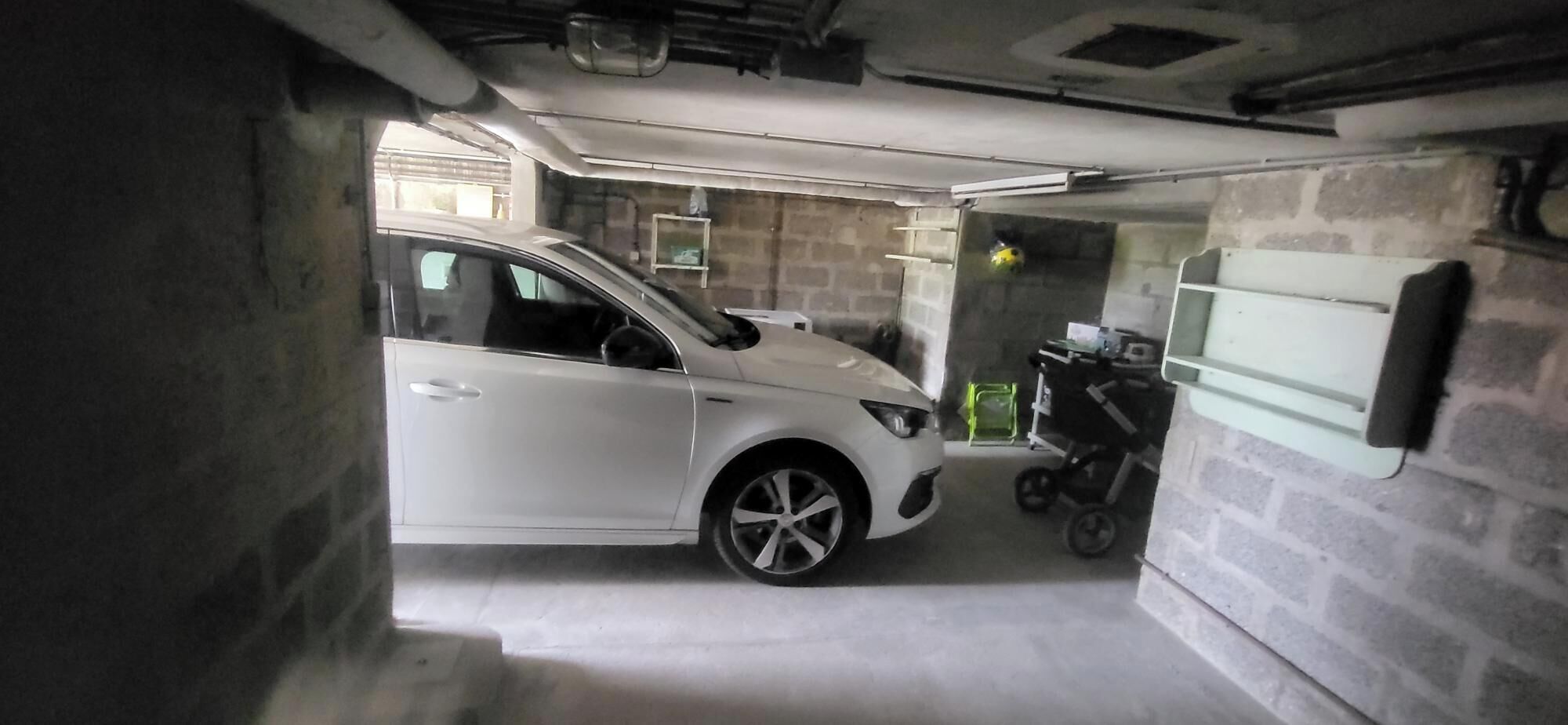 A white car parked in a garage with a stroller and a baby carrier.
