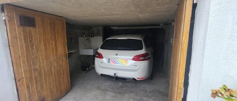 Valkoinen auto oli pysäköitynä pieneen autotalliin, jossa oli puuovi ja laatoitettu seinä.