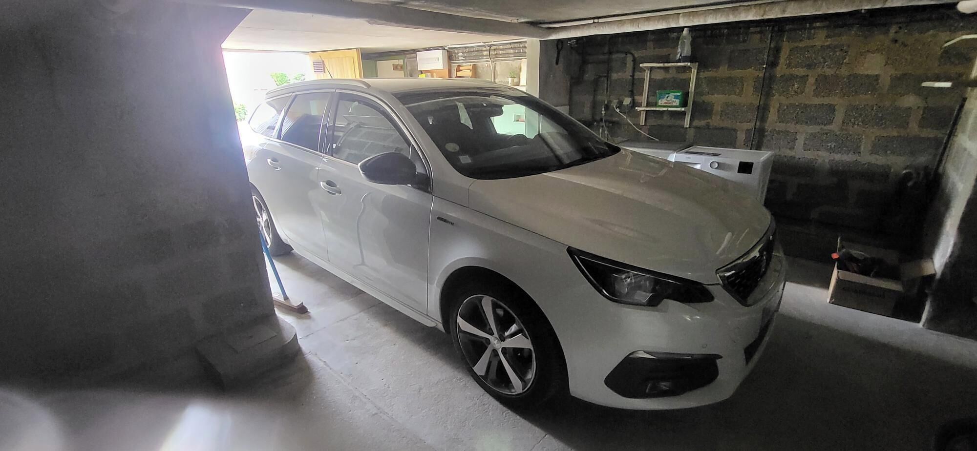 En hvid bil parkeret i en garage med en murstensvæg og en stige.
