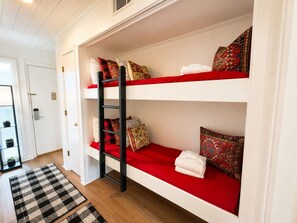 A bunk bed with red bedding and decorative pillows, a black ladder, and a checkered rug on a wooden floor. - Ocean Villas A246-Professionally Managed by HHIB&T Vacation Rentals (Hilton Head Island)