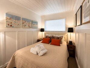 Ein ordentlich gemachtes Bett mit gesteppter Bettdecke, zwei Nachttischlampen und einem Fenster mit Jalousien.