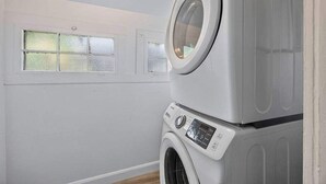 Een wasserette met een voorlader wasmachine en droger, een raam met geëtste glas, en een witte muur.