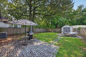Un jardin avec une terrasse, un barbecue et un hamac.