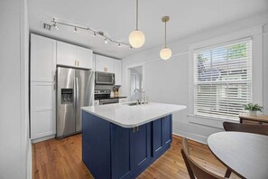 A modern kitchen with white cabinets, stainless steel appliances, a blue island, and pendant lighting. - The Dellwood Cottage - Near Local Shops & Eats (Jacksonville)