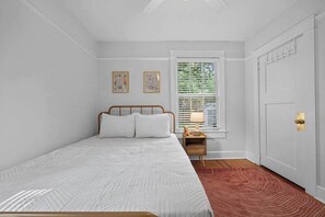 Ein Schlafzimmer mit einem Bett, einem Nachttisch, einem Fenster mit Jalousien und einer Tür.