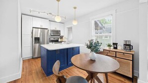 Een moderne keuken met een centraal kookeiland, roestvrijstalen apparatuur en een eethoek met een ronde tafel.