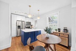 A modern kitchen with a central island, stainless steel appliances, and a dining area with a round table. - The Dellwood Cottage - Near Local Shops & Eats (Jacksonville)
