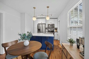 Eine moderne Küche mit weißen Schränken, einer blauen Kochinsel, Edelstahlgeräten und einem Essbereich mit Holztisch und -stühlen.