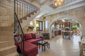 A spacious living area with a red sofa, a staircase, and an open kitchen area with stone walls. - Villa Freedom | A Private Luxury Estate in the Heart of Crete (Chania)