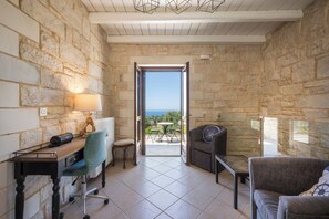 A room with stone walls, a desk with a lamp, a chair, a sofa, and a view through an open door to the outdoors. - Villa Freedom | A Private Luxury Estate in the Heart of Crete (Chania)